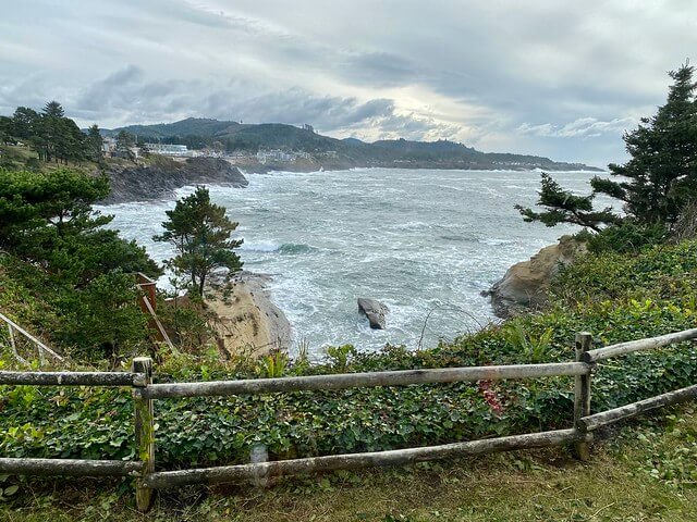 Depoe Bay ocean view from behind the wood fence. Coastal pine trees frame the view. 