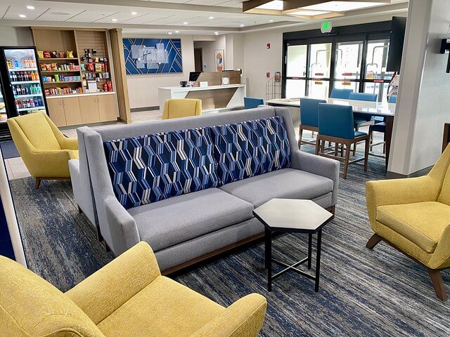 Holiday Inn Express Grand Junction hotel lobby with yellow chairs, grey sofas. Snack room to left of hotel reception desk with hotel logo behind reception desk. 