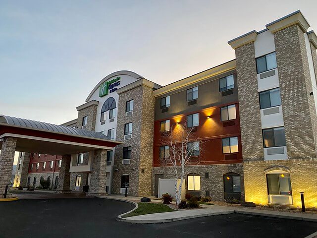 Holiday Inn Express & Suites Grand Junction hotel exterior at sunset. Brick facade with hotel logo on front of beige stucco and brick building with arched portico.