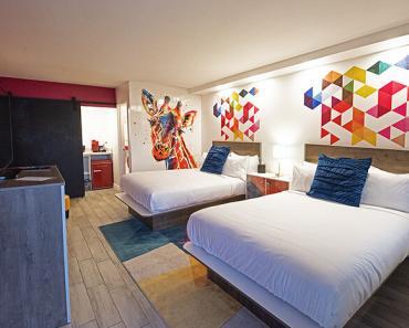 Two queen beds in a room with brightly colored wall murals, including a giraffe painting