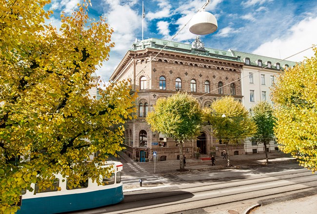 Three-story Elite Plaza Hotel brick building exterior. Two trees, with fall colored leaves, front the 19th century building. An electric street car is about to pass by the luxury Gothenburg hotel.