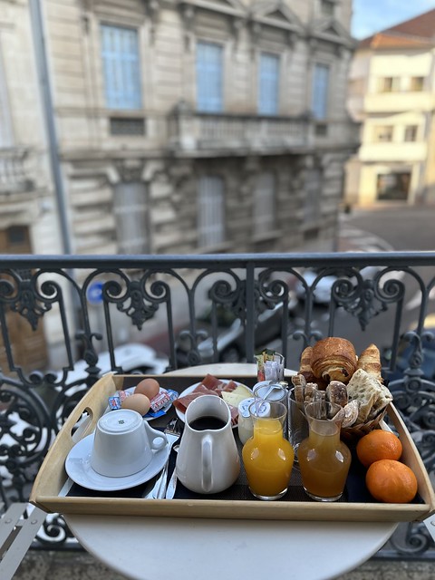 Breakfast tray on hotel balcony with basket of pastries, coffee, juice, 2 oranges, meats, cheese and 2 hardboiled eggs.