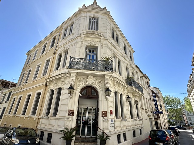 Three-story Hotel La Residence entrance. The classic-style hotel has a third floor balcony with a small palm tree on the right side of the balcony, above the hotel entrance.