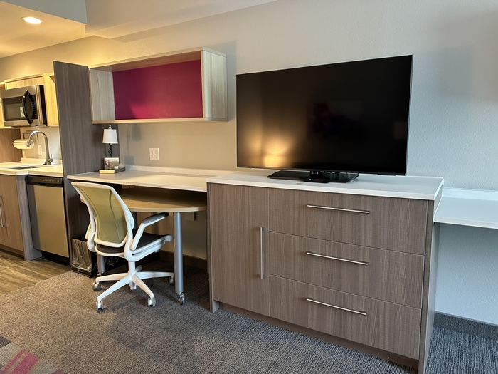 A dresser, tv, desk and chair in a room.