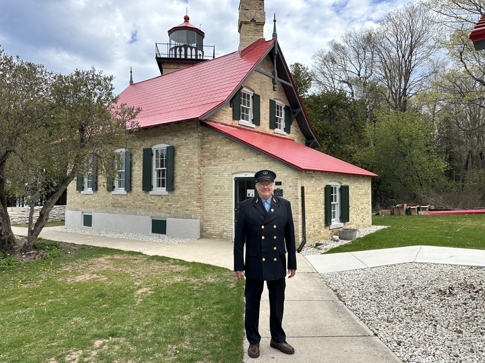 A man in uniform standing in front of a lighthouse. 