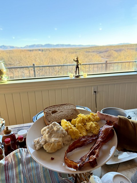 Breakfast plate of wheat toast, biscuits with gravy, scrambled eggs, and 2 strips of bacon. A miniature toy cowboy is on the sill of the large picture window looking out to the yellow leaves on the trees and the Arizona mountains in the distance. 